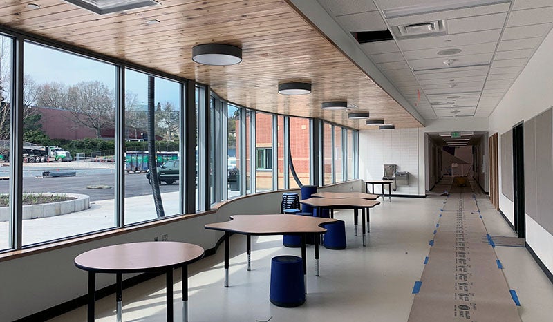 a hallway with tables in front of a curving wall of windows on the left