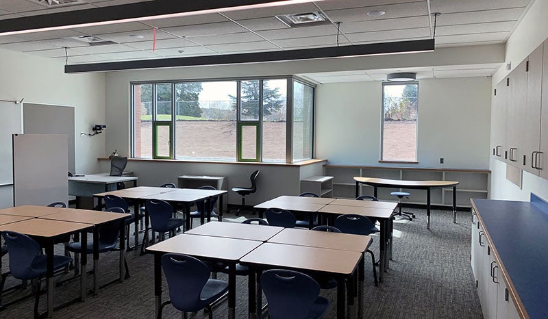 a room has groups of desks, windows and chairs