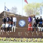 A group of students sits together near the Hampton University sign