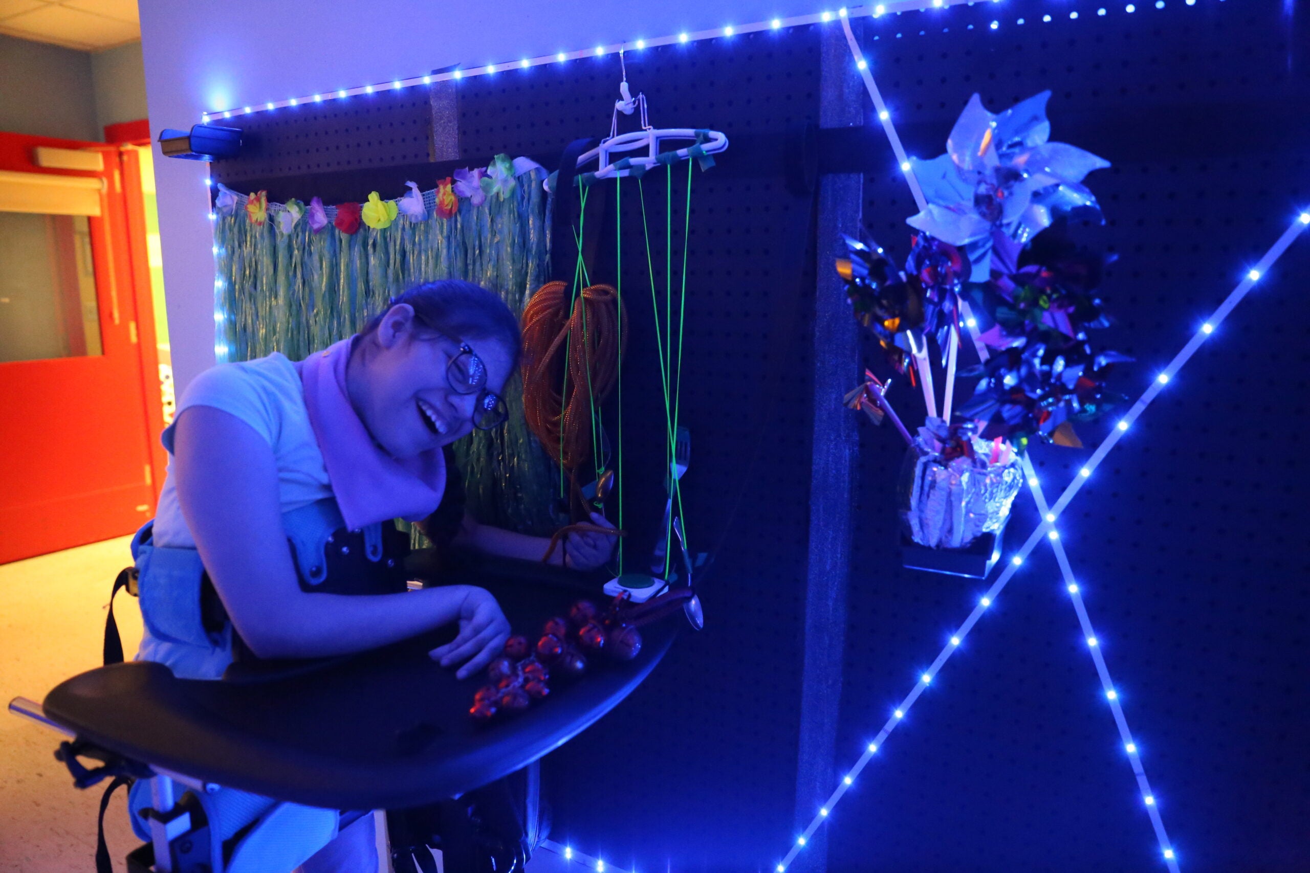 Student with glasses pulling on strings and playing with bells on the sensory wall