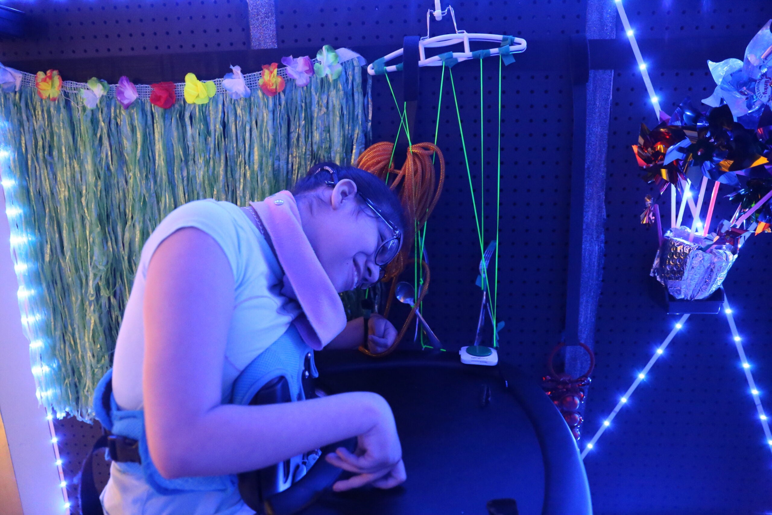 Student with glasses smiles and plays with the sensory wall.