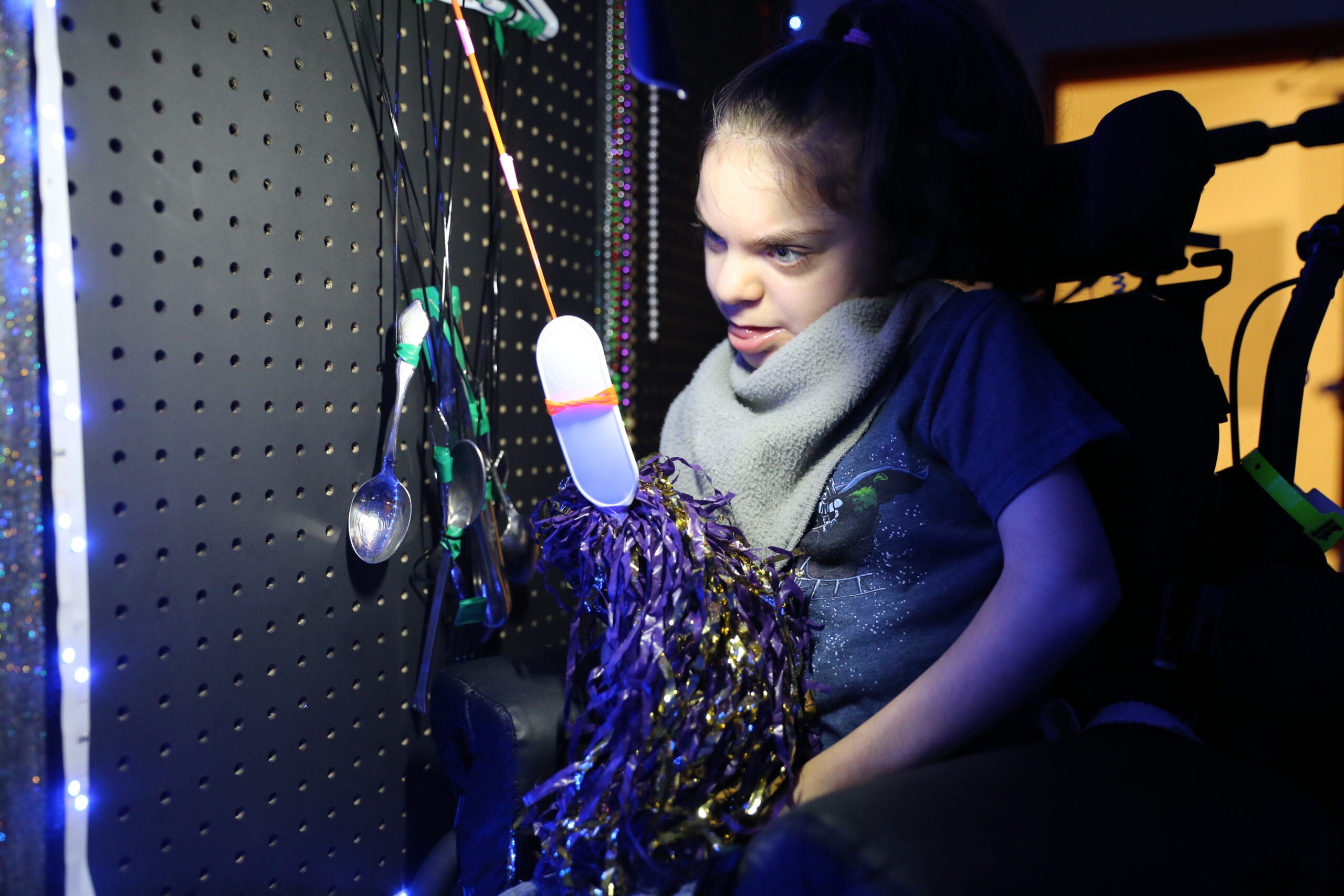 Student playing with pom pom and spoons on sensory wall. 