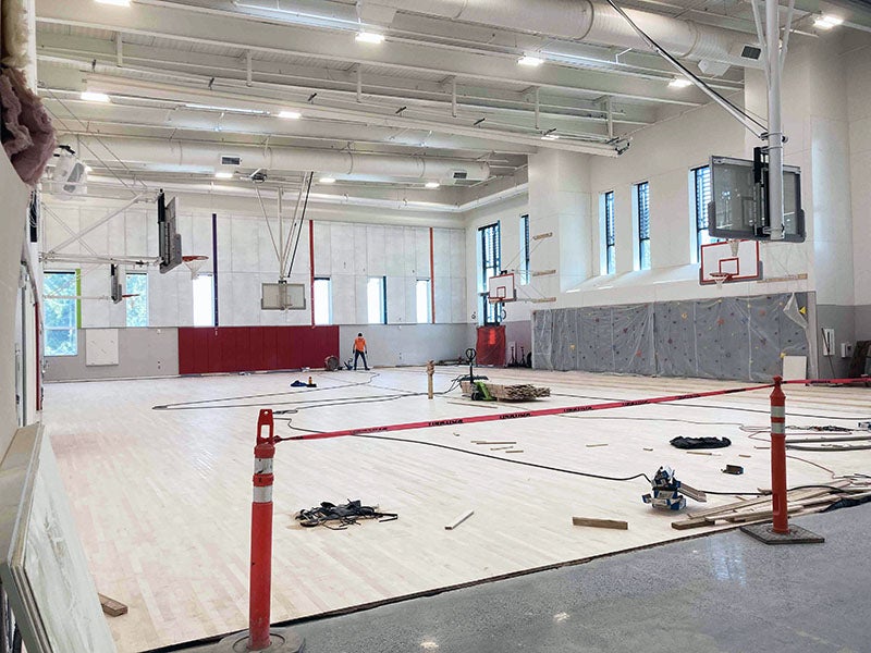 a large two-story room has backetball hoops and a wood floor is being installed