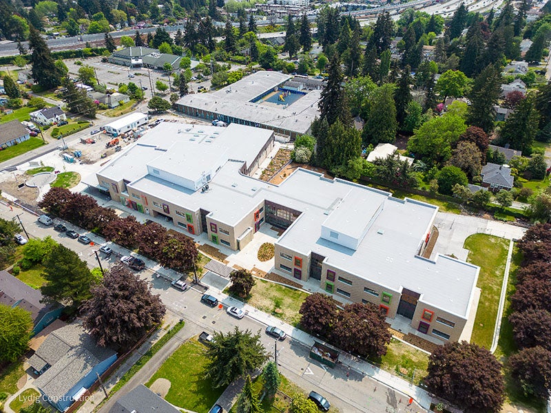 aerial view of a large building with trees along the street and grass planted between the trees and the school building. another large building can be seen in the center top