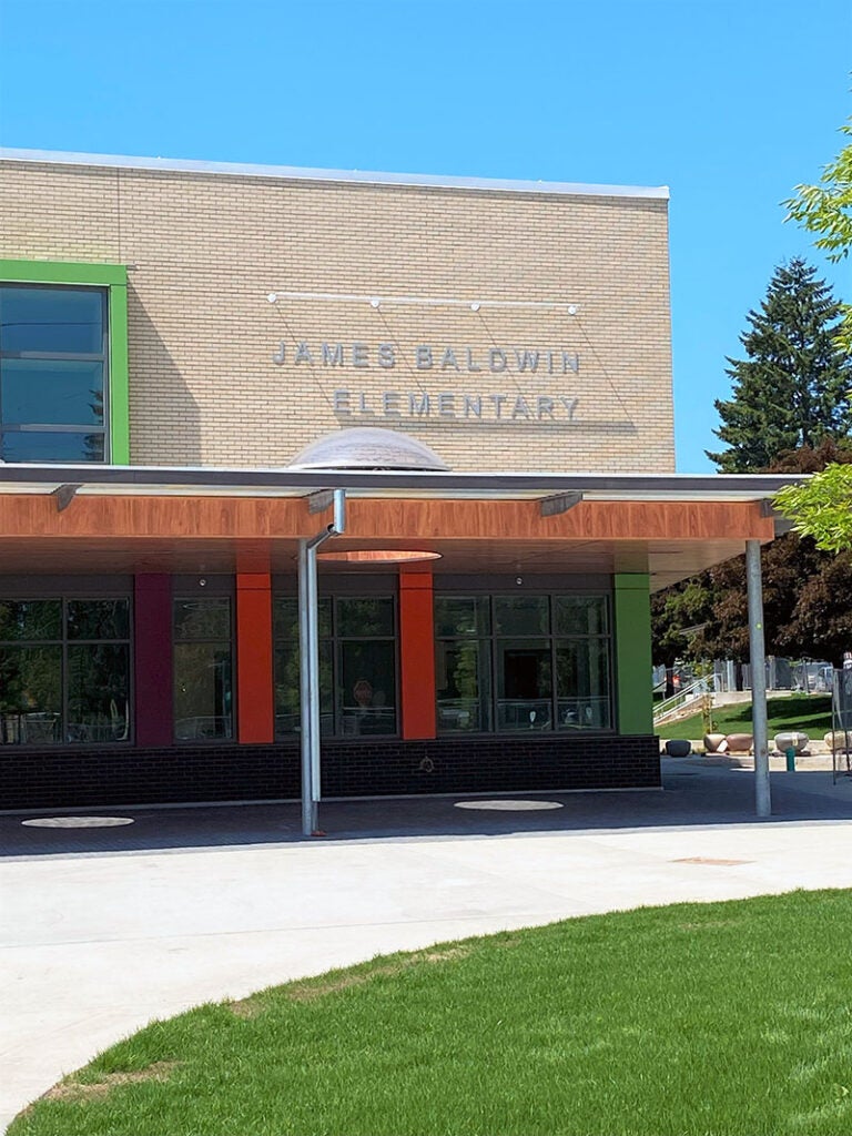 part of a two story building with a canopy that has wood edge and windows. a sign on the building says James Baldwin Elementary
