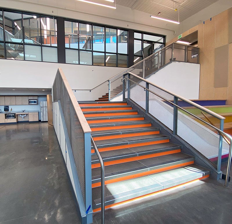 an interior stair leads up from a concrete floor past a group of windows. there is a slide next to the stairs