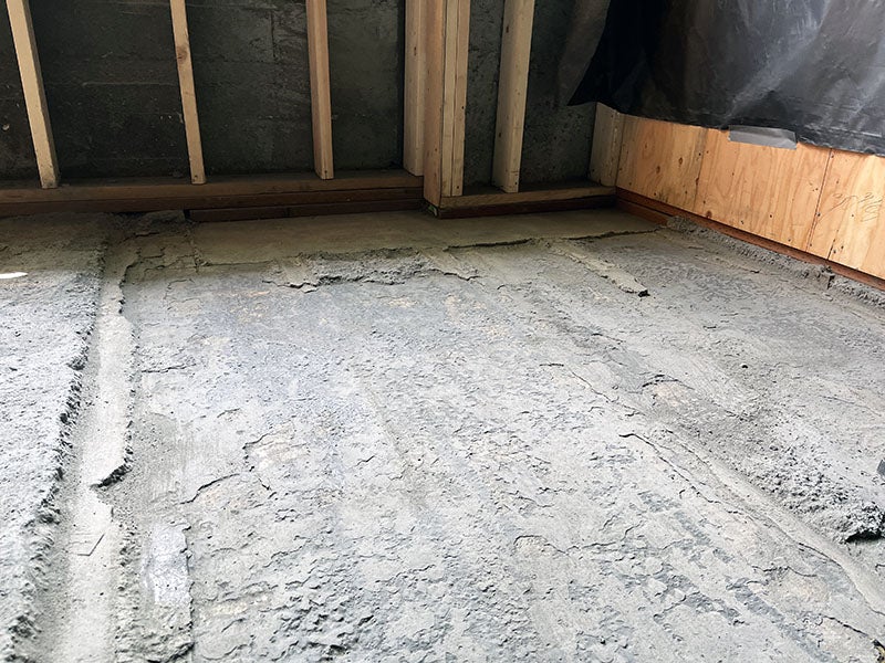 a rough concrete floor with a wall that has studs in place