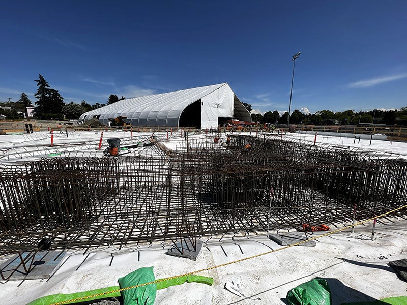 rebar formed into tall grids sits in foreground on top of a white material. a large tent is in the background