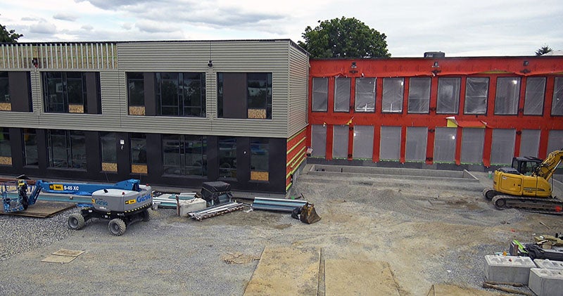 a building with metal siding and windows on part and orange underlayment and plastic in the window openings on another part