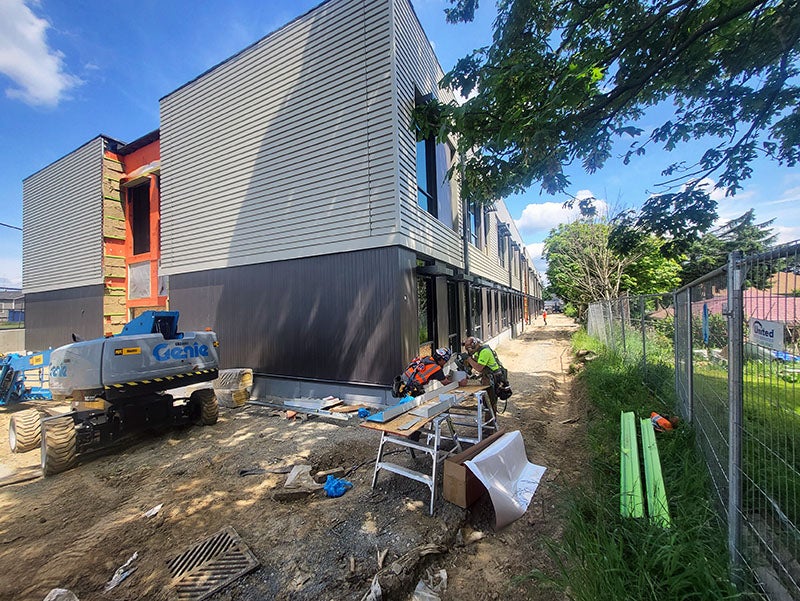 the corner of a two-story building has metal siding vertically in a dark color at the bottom and horizontally in a lighter color above