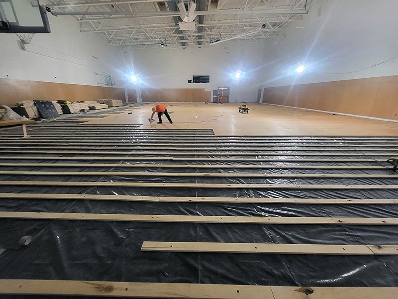 a large room with high ceilings has a worker installing wood planks for a floor