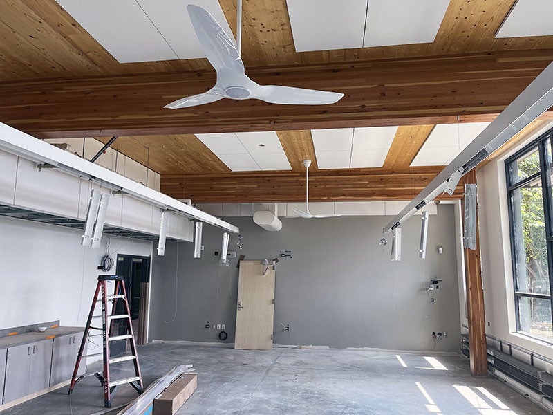 a room with windows on one wall and wood beams with a ceiling fan and partially installed light bars