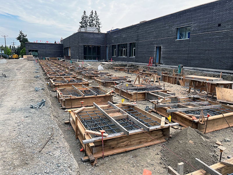 square concrete forms with rebar are in front of a brown brick building