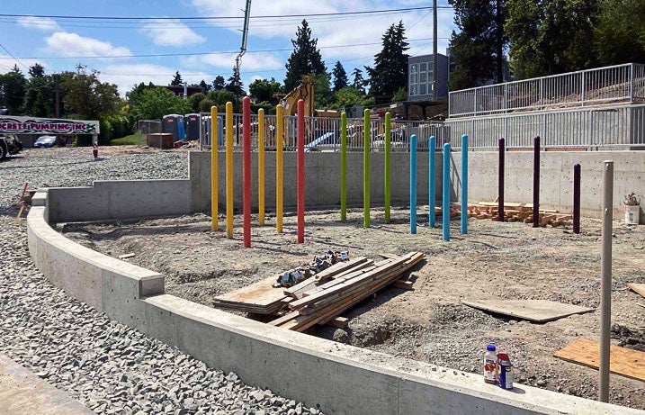 a concrete curb separates gravel from soil. multi colored posts stick up out of the soil