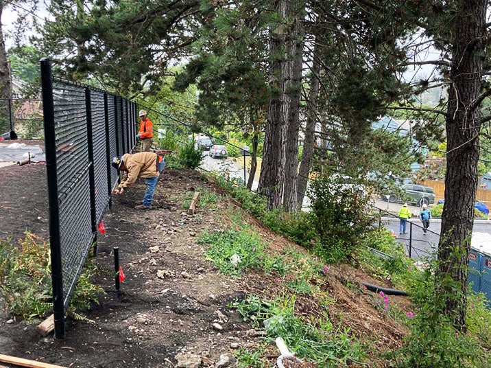 a person is at the top of slope that has trees and other vegetation. the person is bent over in front of a black metal fence