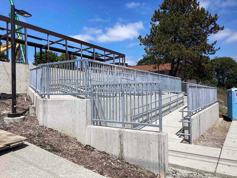 a concrete ramp zig zags on a hill with concrete short walls with metal railings and fence