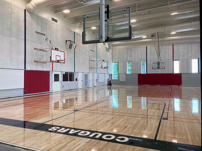 an empty gymnasium with basketball hoops, floor striping, and the word Cougars on the floor