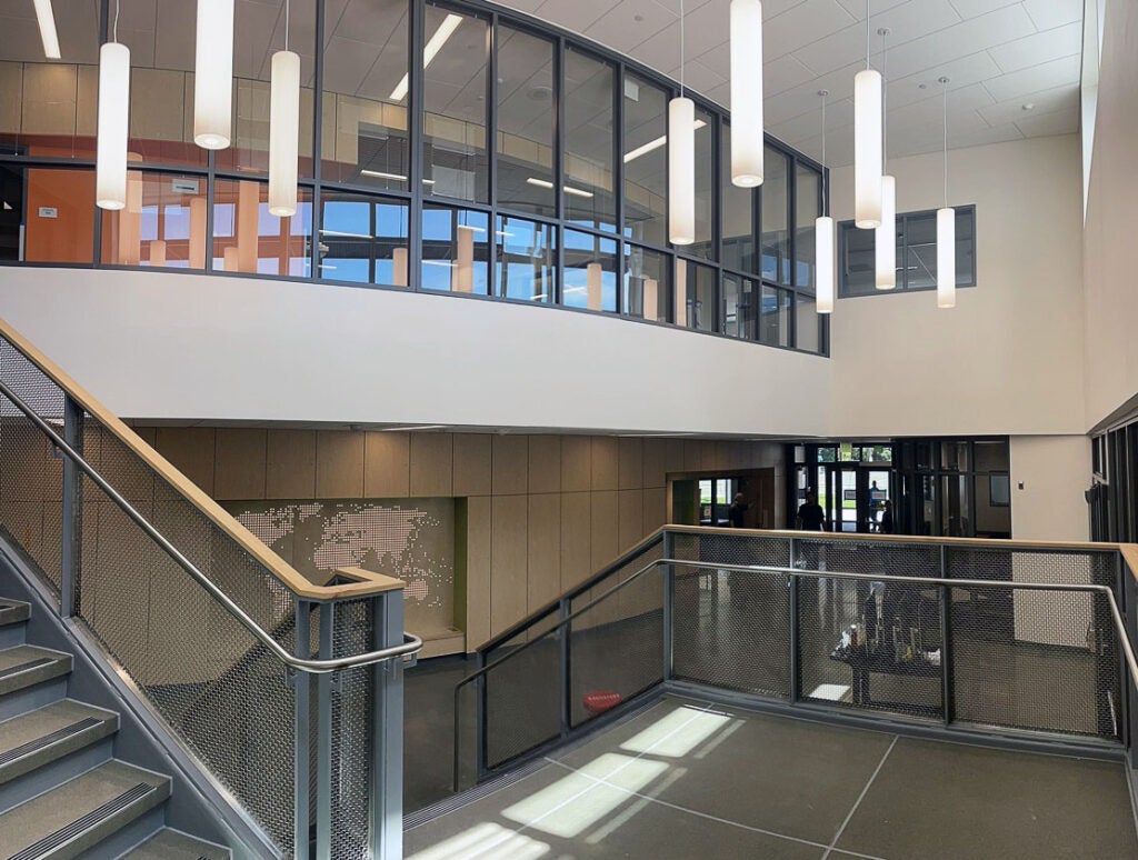 view from halfway up stairs on a landing. you can see part of the second floor with a curved glass wall and part of the lower floor.