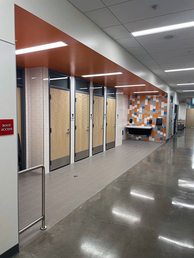 part of a hallway with doors set back from the path by tile. a sink hangs on the wall at one end