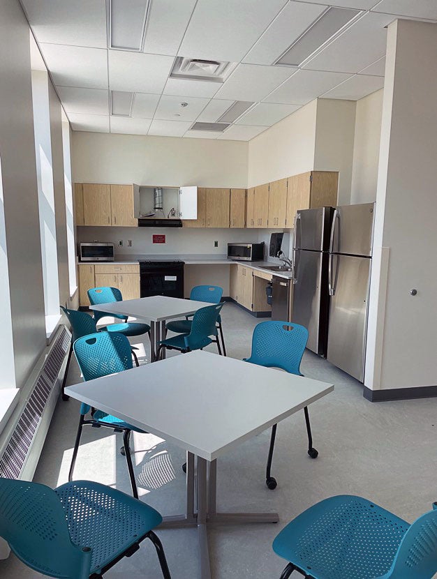 a room with two refrigerators, cabinetry, a stove, two microwaves, and some tables and chairs