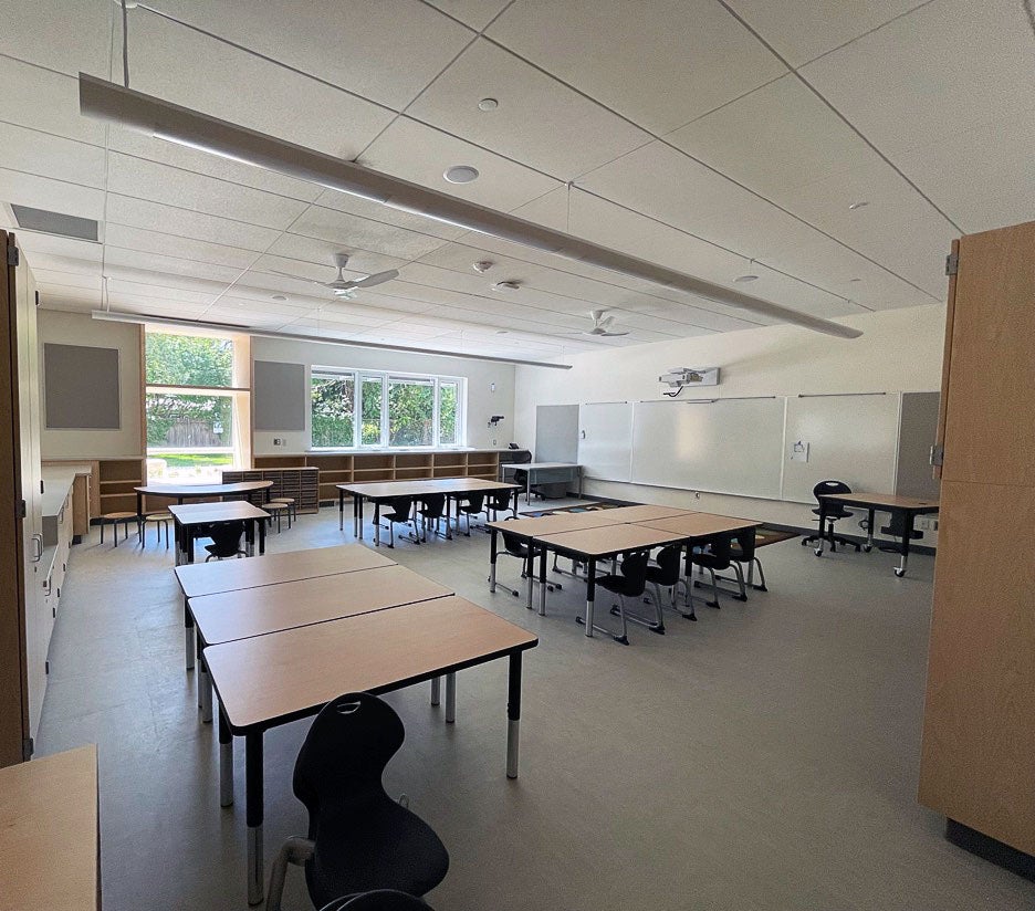 a classroom has groups of tables with chairs, bookcases, whiteboards, lighting and ceiling fans