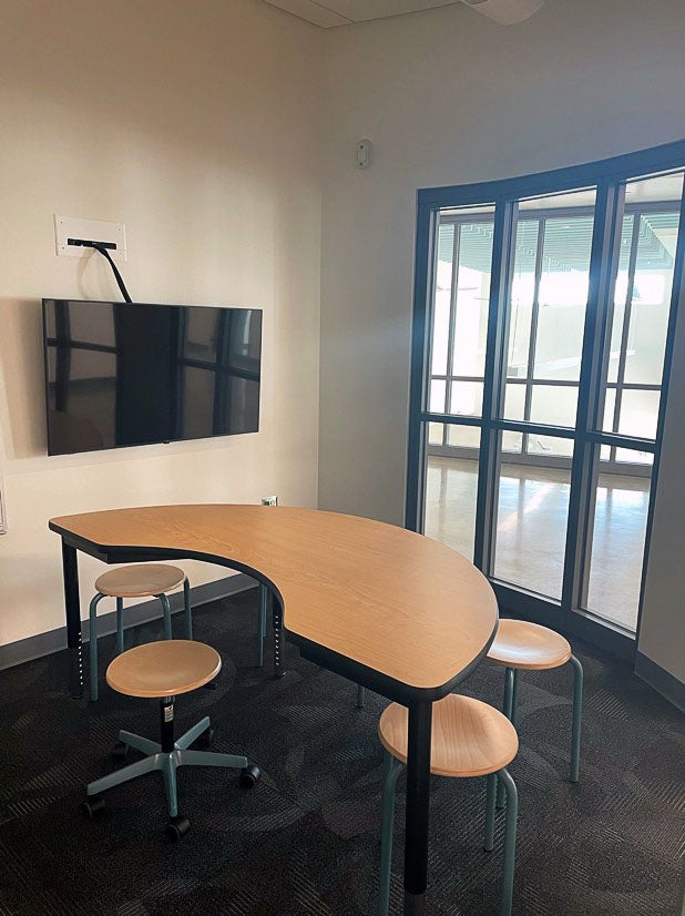 a small room with a video screen, windows on one wall, a half circle table and five stools