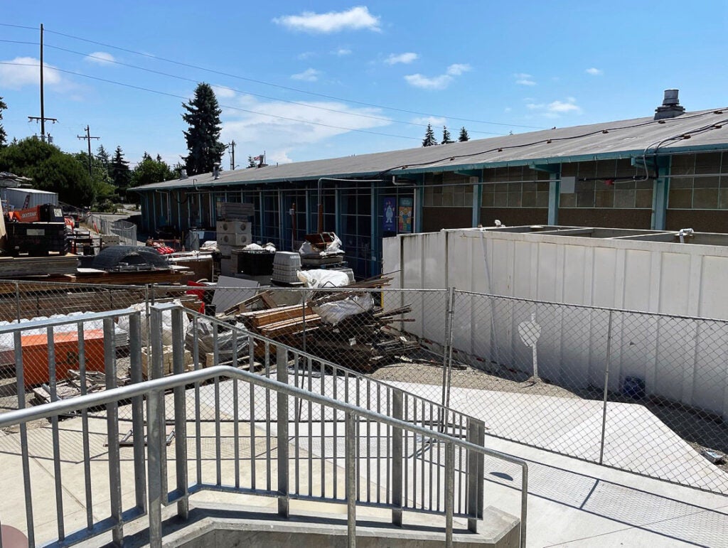 outdoor looking toward a long low building with a stairway, concrete walk, and construction materials in front of it