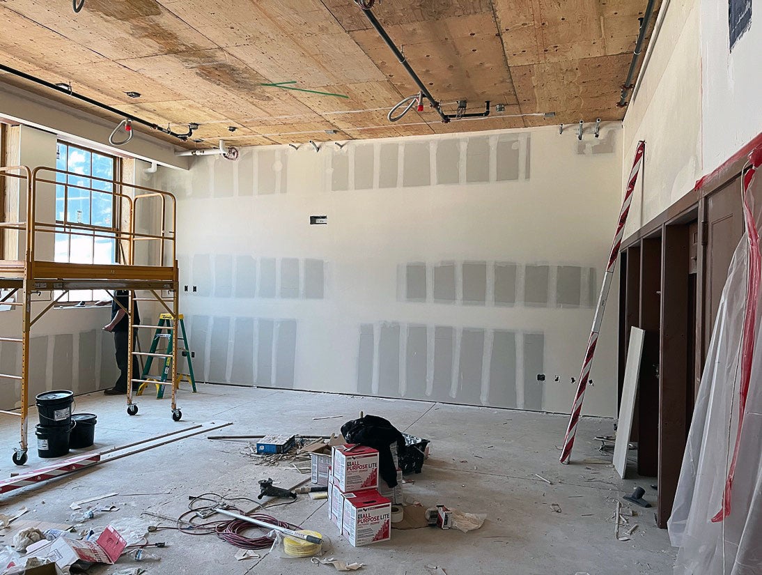 a room has a wood ceiling. the walls are wallboard with tape and mud installed. There is a window on the right and doors on the left