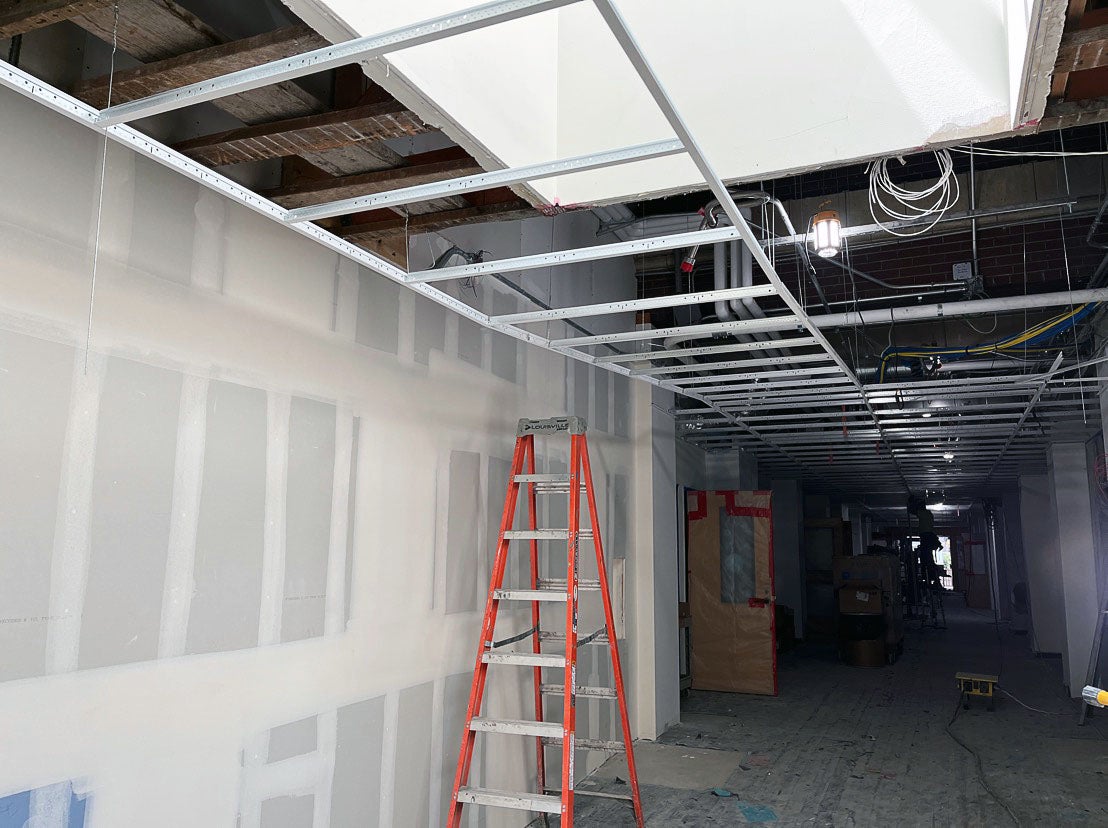 an unfinished hallway with one wall showing wallboard that is taped and mudded. The ceiling is open with a metal grid partially installed