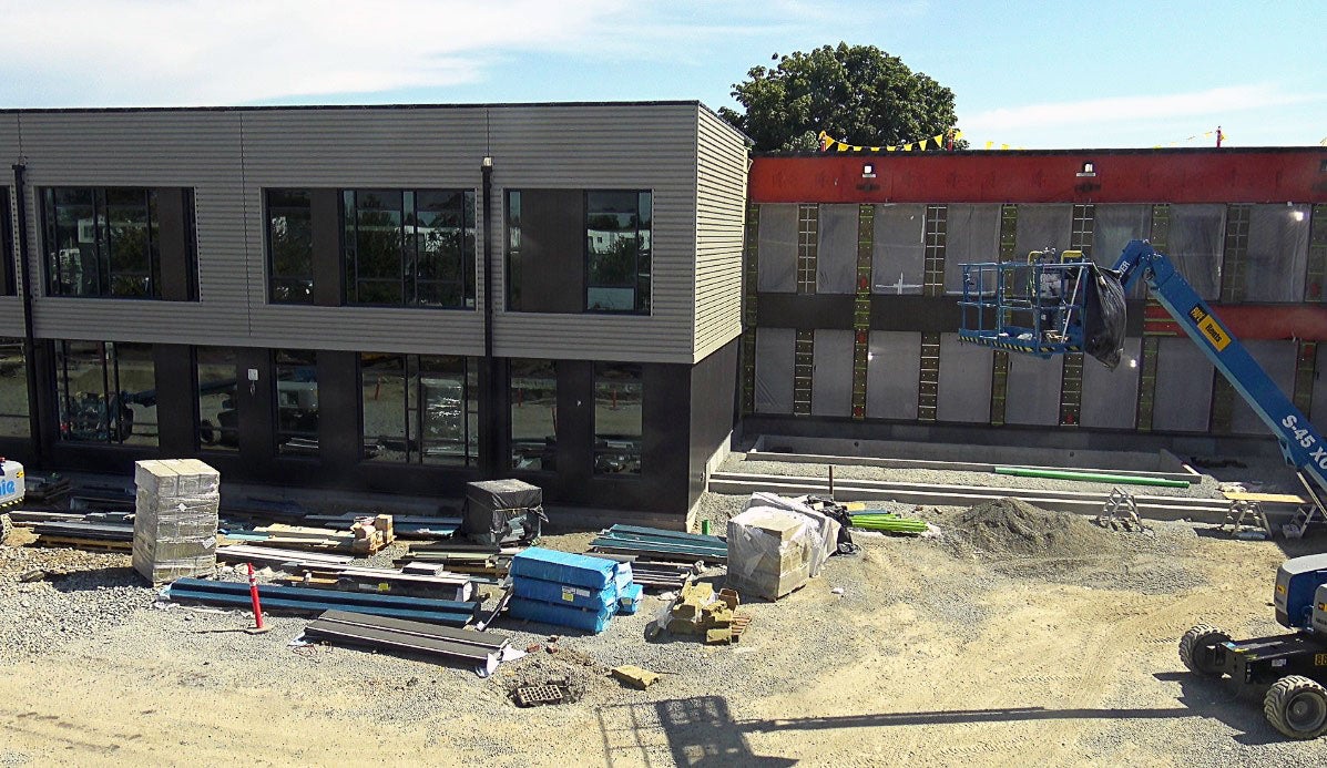 a 2 floor building has two parts one is more forward and has brown and cream siding, windows; the other is back and has orange underlayment and plastic over the window holes