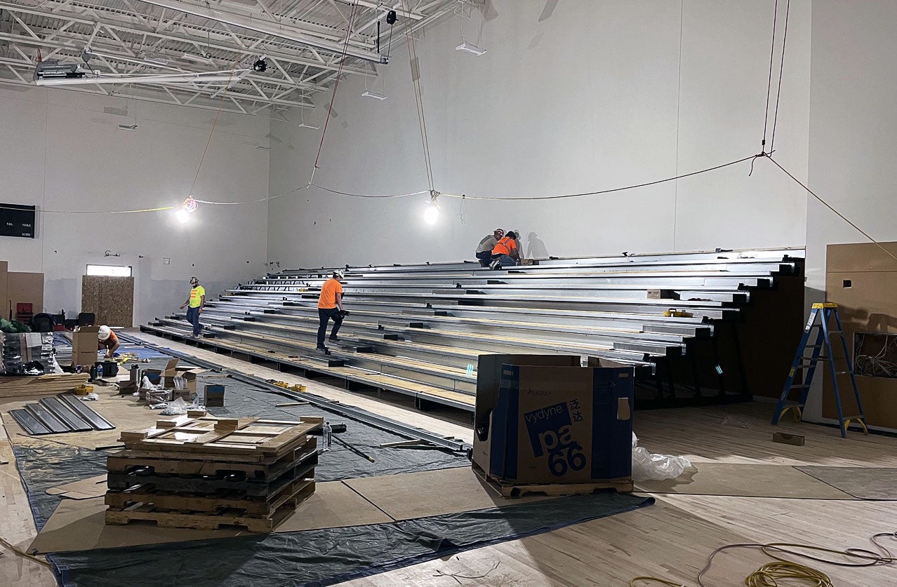 workers are installing bleachers in a large room with a high ceiling