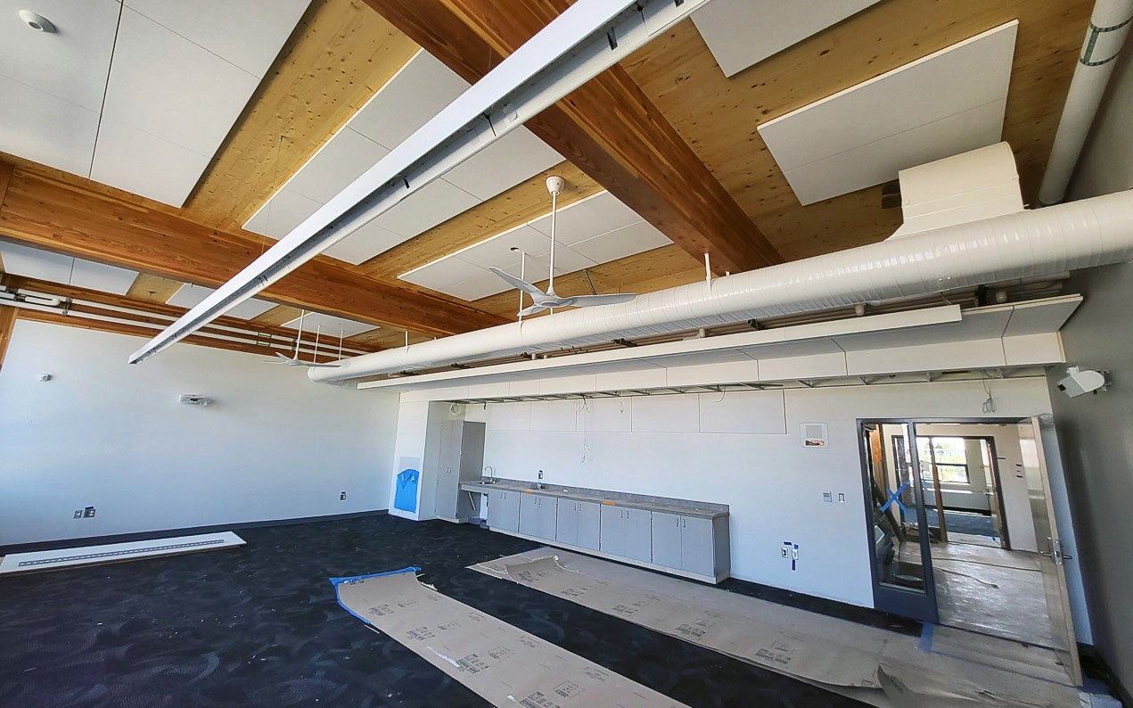 looking up toward the ceiling of a room that has glue lam beams and cross pieces of lighter colored wood - lighting fixtures are partially installed