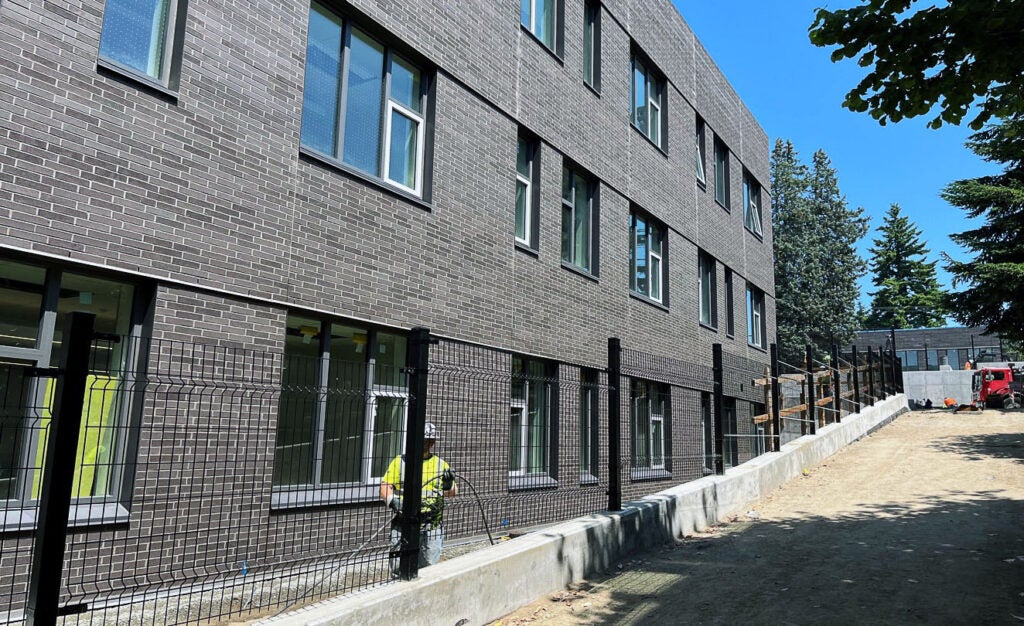 part of a 3-story brick building with a black fence behind a curb