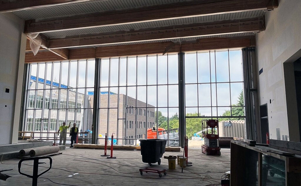 a two-story glass window wall is being installed. construction equipment can be seen and a large brick building is outside the window