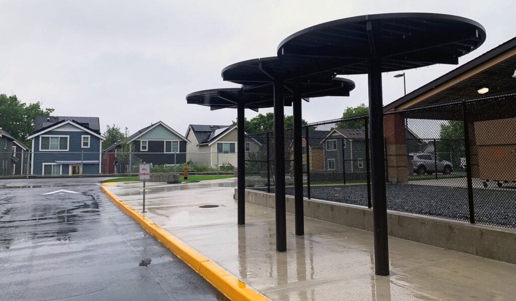 a canopy made of three circles on metal poles is above a sidewalk with a yellow painted curb