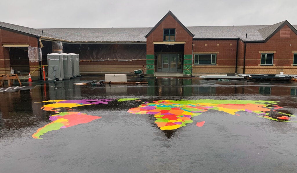 a brick building has a world map painted on the blacktop in front of it