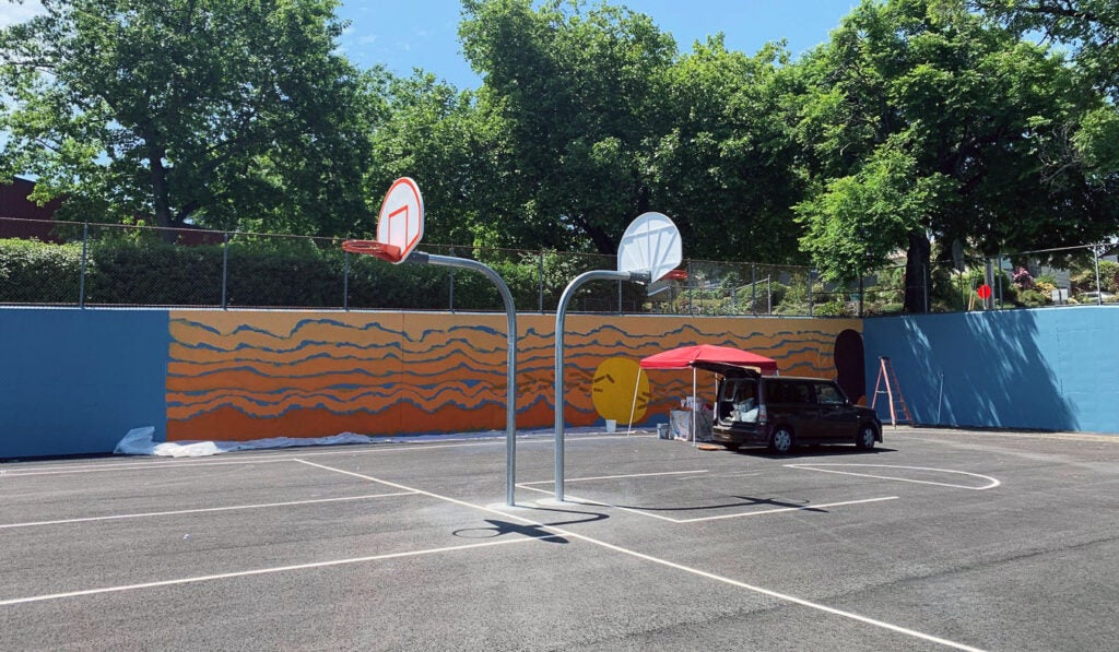 a mural is being painted on a blue wall surrounding a basketball court