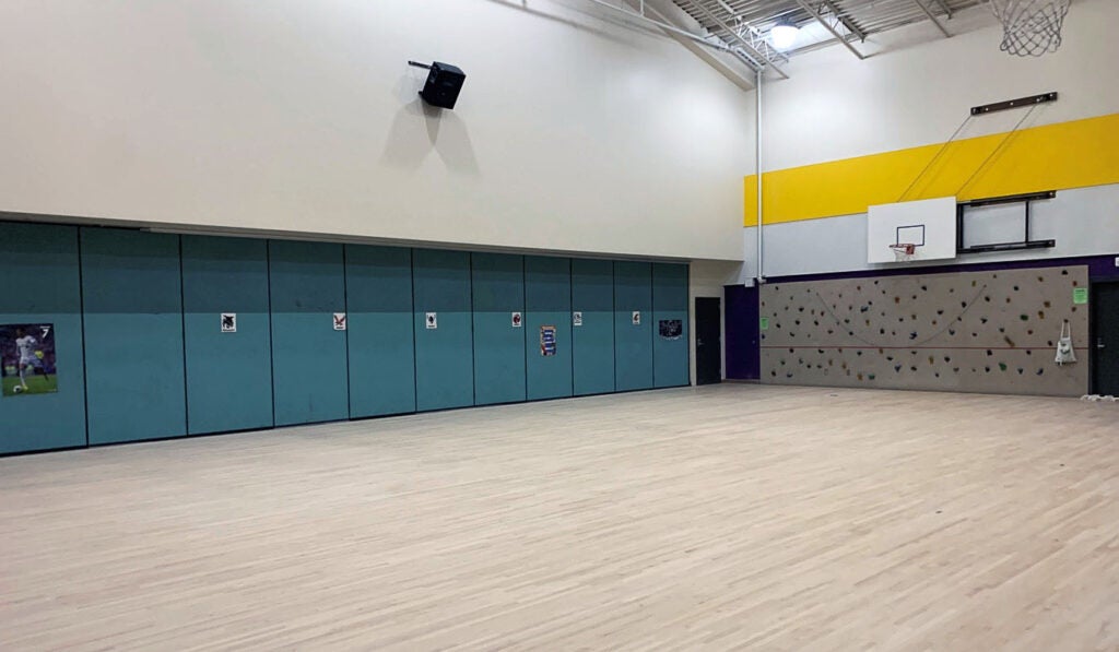 a large room has a climbing wall and a basketball hoop - the wood floor is unfinished