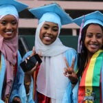 Three graduates smile for a photo in cap and gown