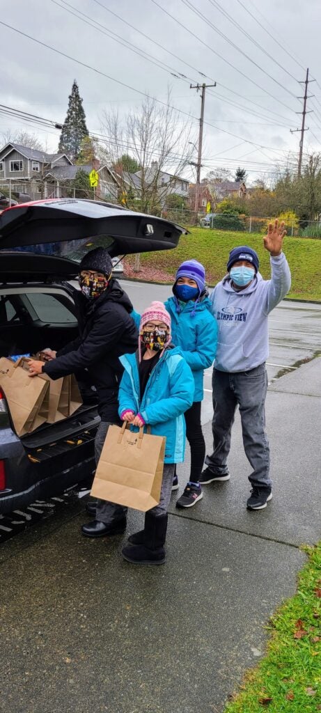 Volunteer parent and her children taking groceries from the car