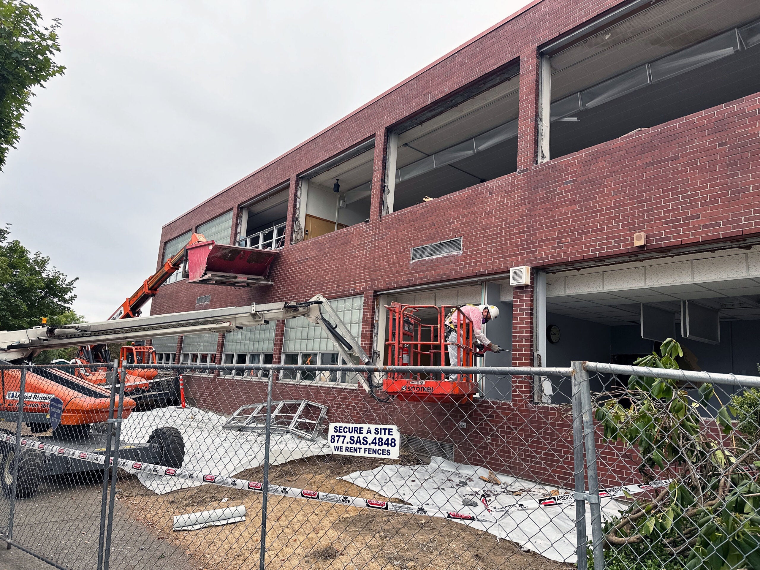 exterior of a 2 story brick building has a person on a lift wearing a mask and removing material from a window frame