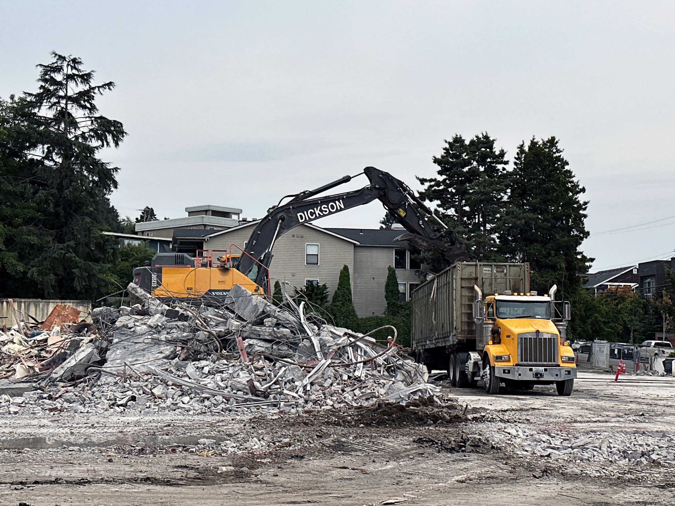 an excavator is on top of a pile of concrete rubble emptying into a container on a truck