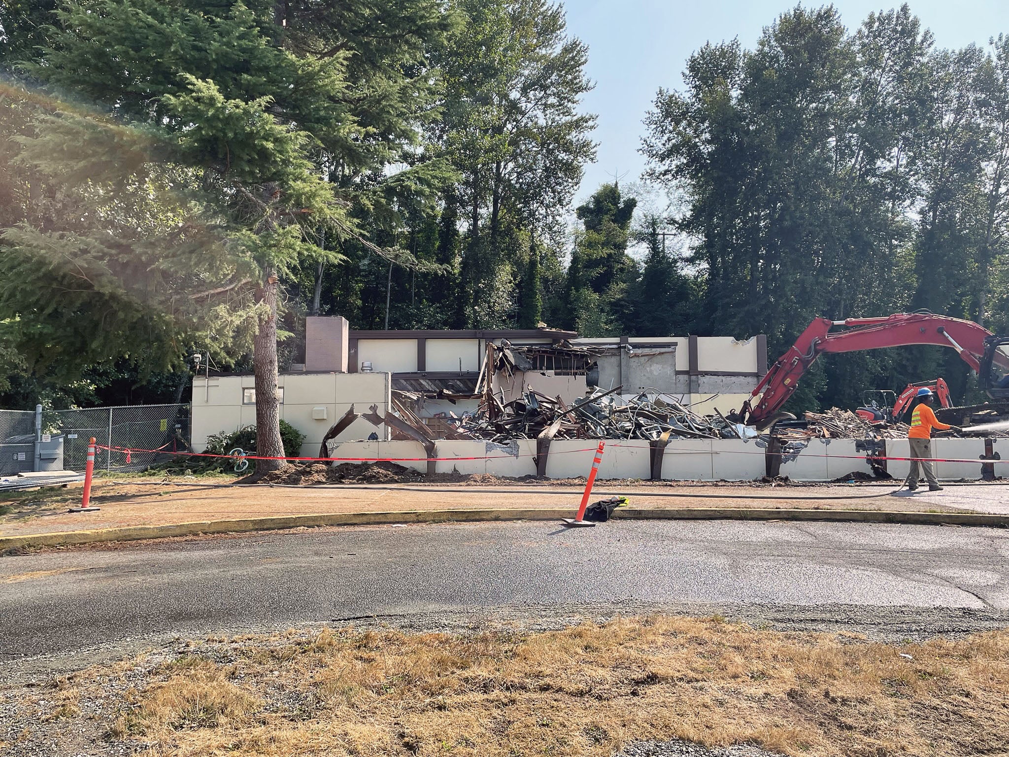 an excavator is demolishing a building with a person spraying a hose