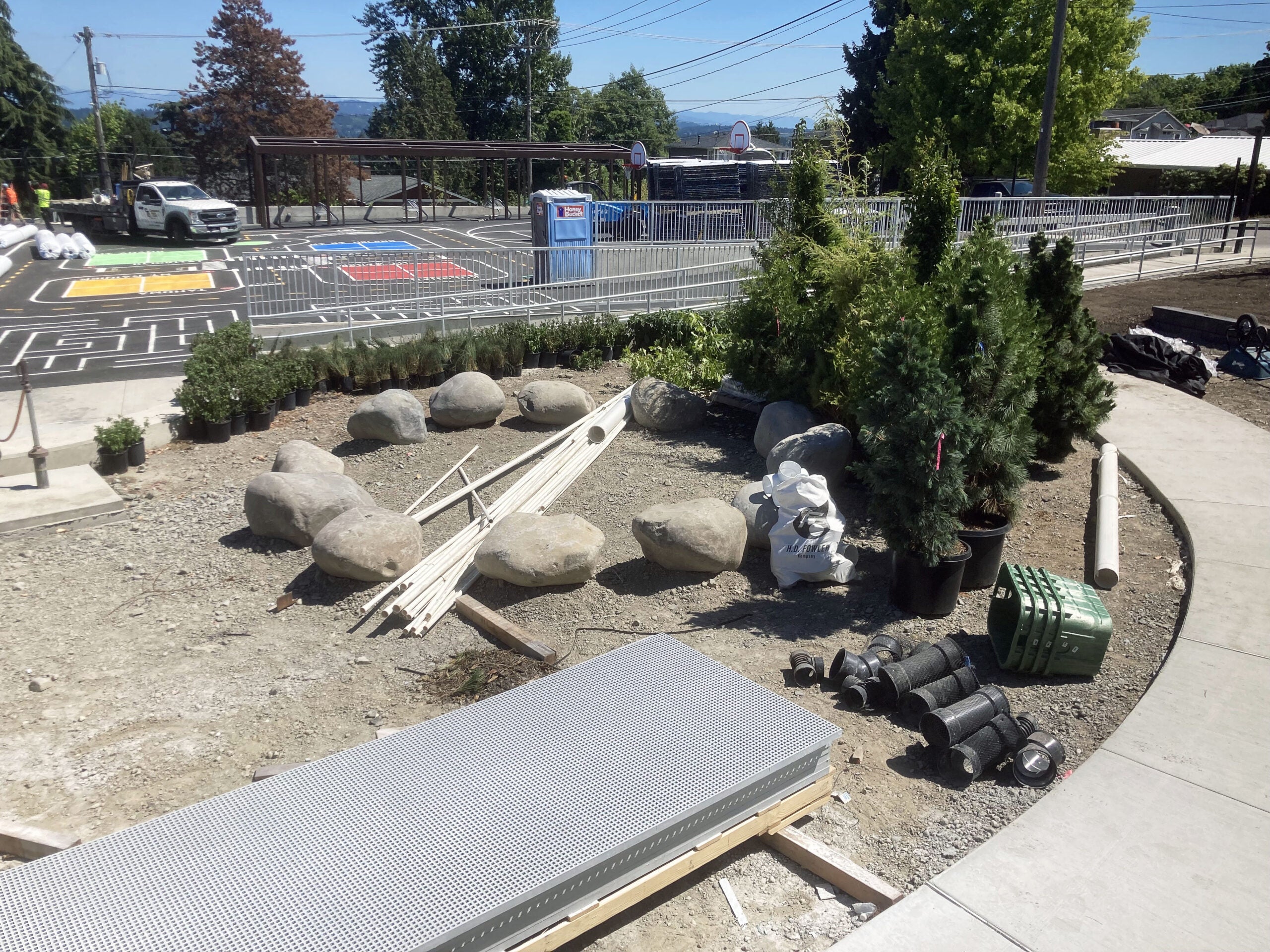 bushes and plants in pots site next to a circle of boulders with a curved sidewalk and a paved area with painted lines