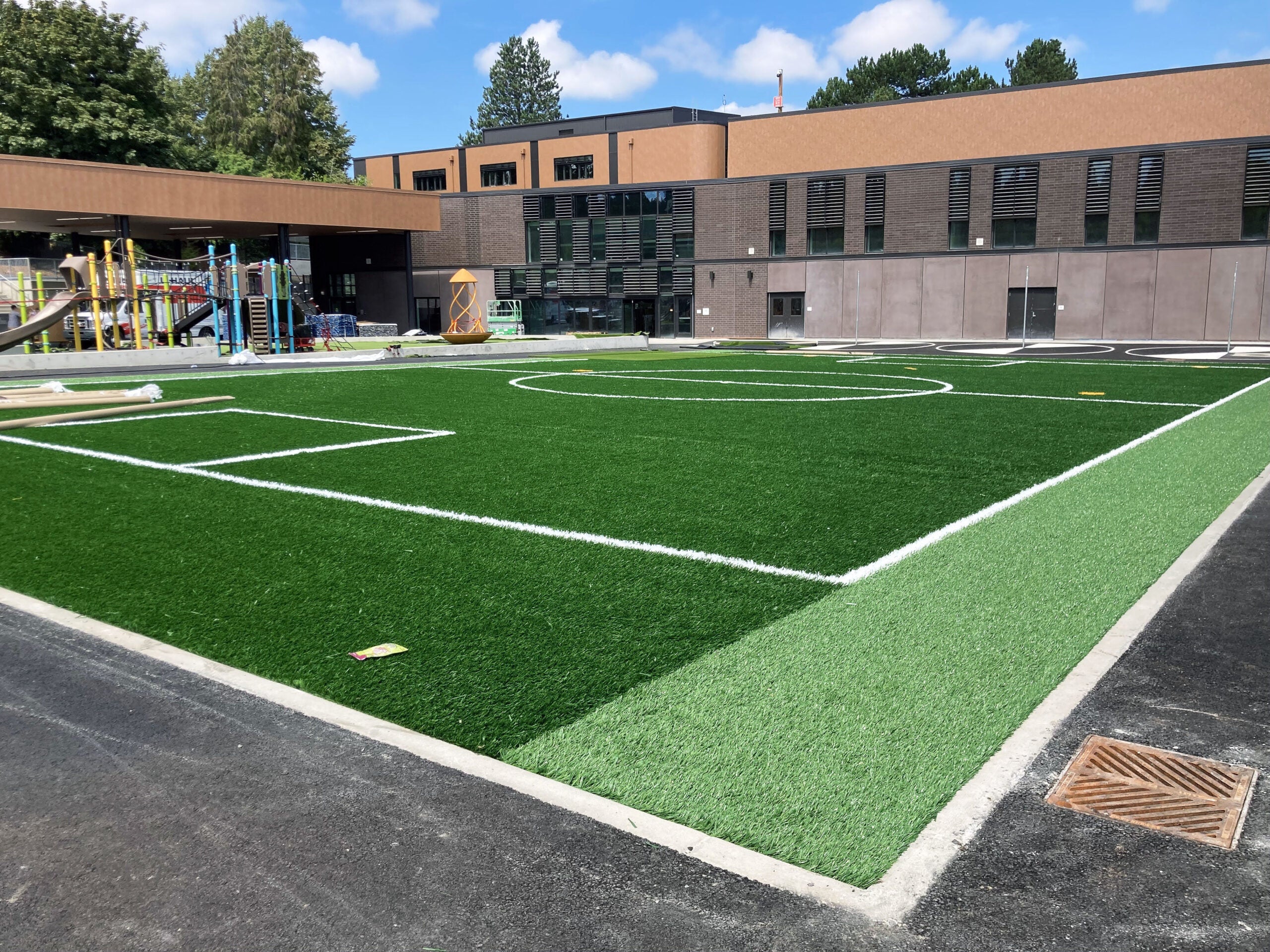 an green turf area with soccer markings is in front of a building with playground equipment behind it
