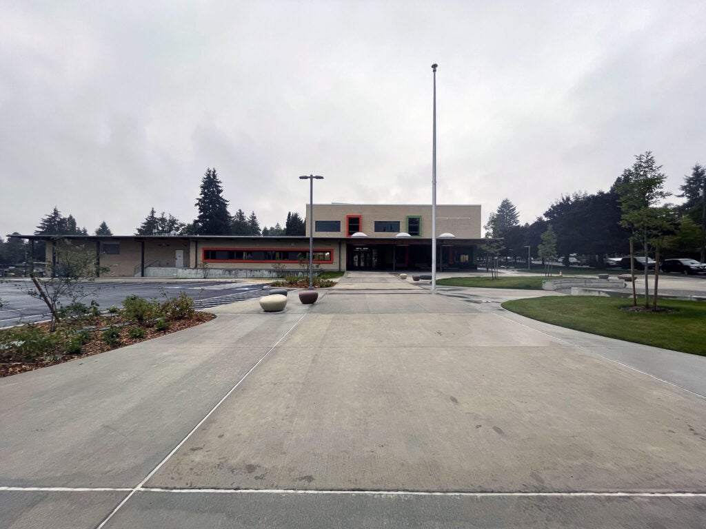 looking up a walkway toward a one and two story building with a covered entry and window frames that are orange and green