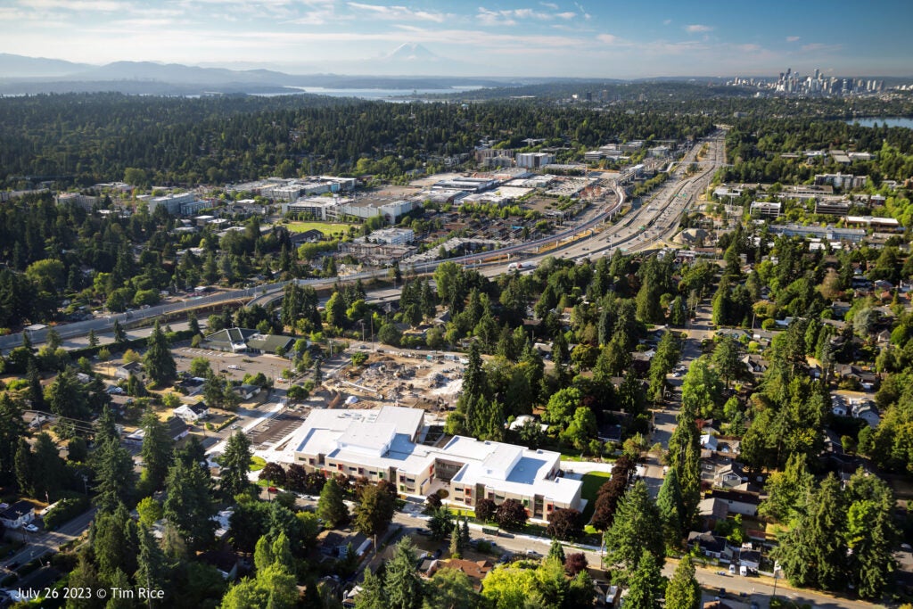 aerial view of a large building with a white roof with a construction area behind it. the freeway can be seen in the background