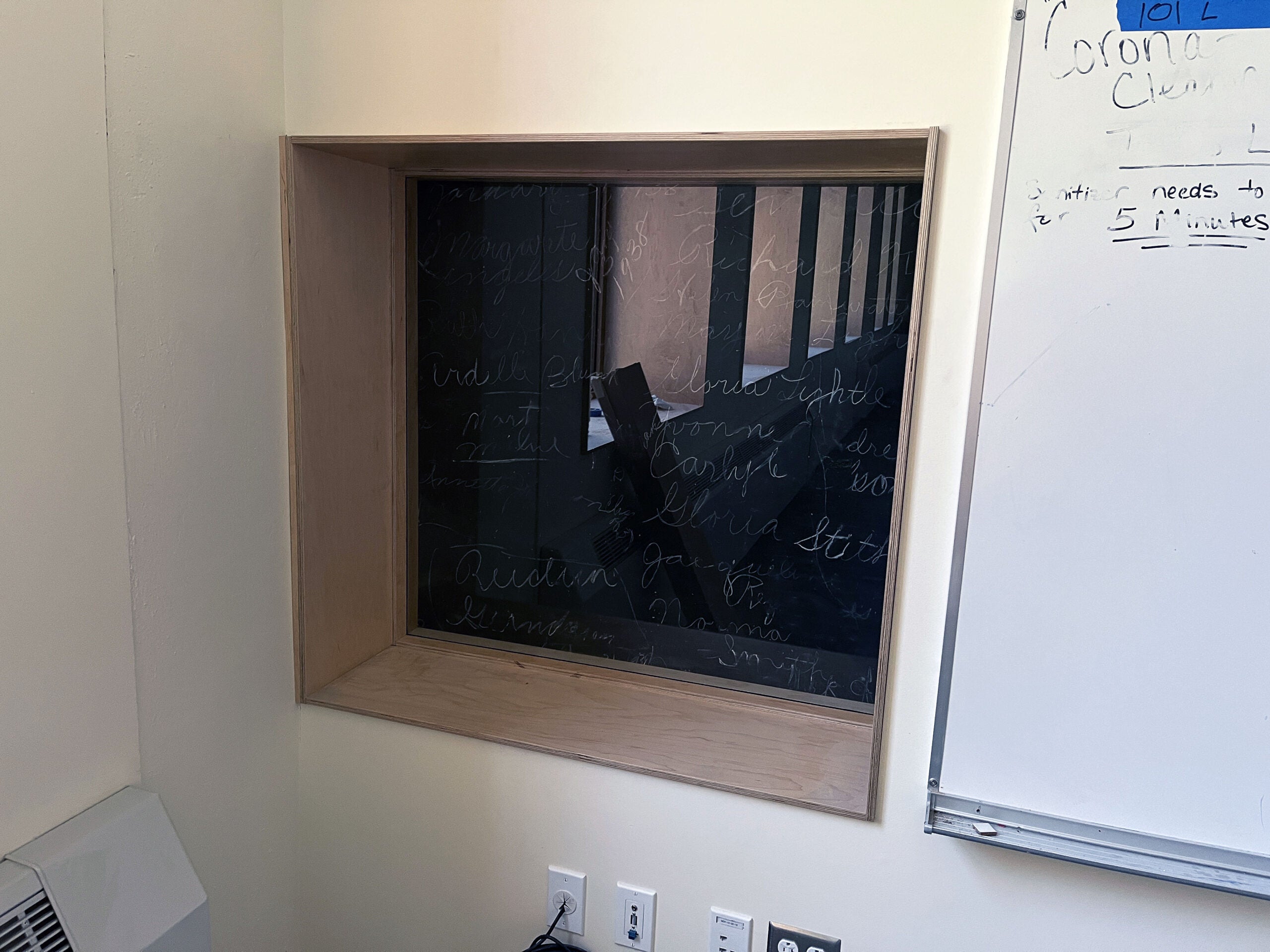 a window is inset into a wall and has a black surface with chalk writing behind the plexiglass