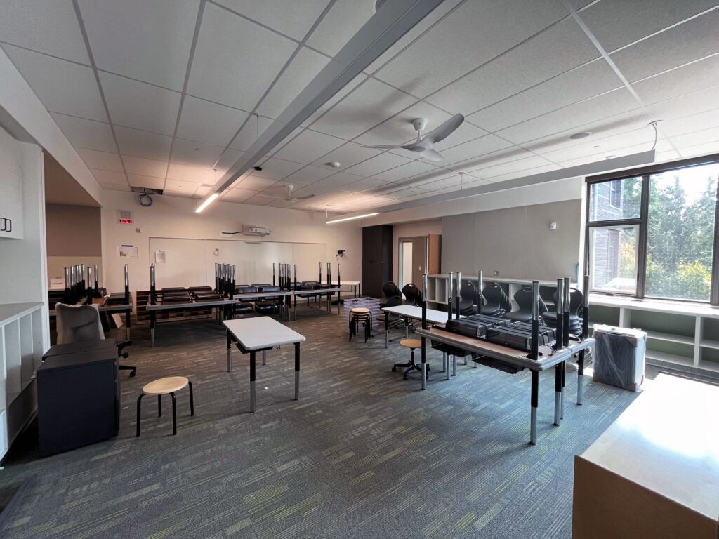 a classroom with tables and chairs stacked and a window with a bookcase below it