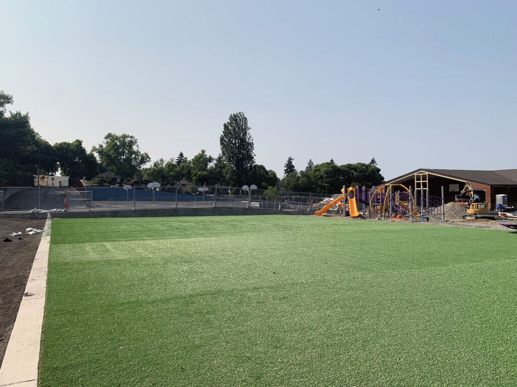 a broad expanse of artificial turf with a baskeball play are behind it